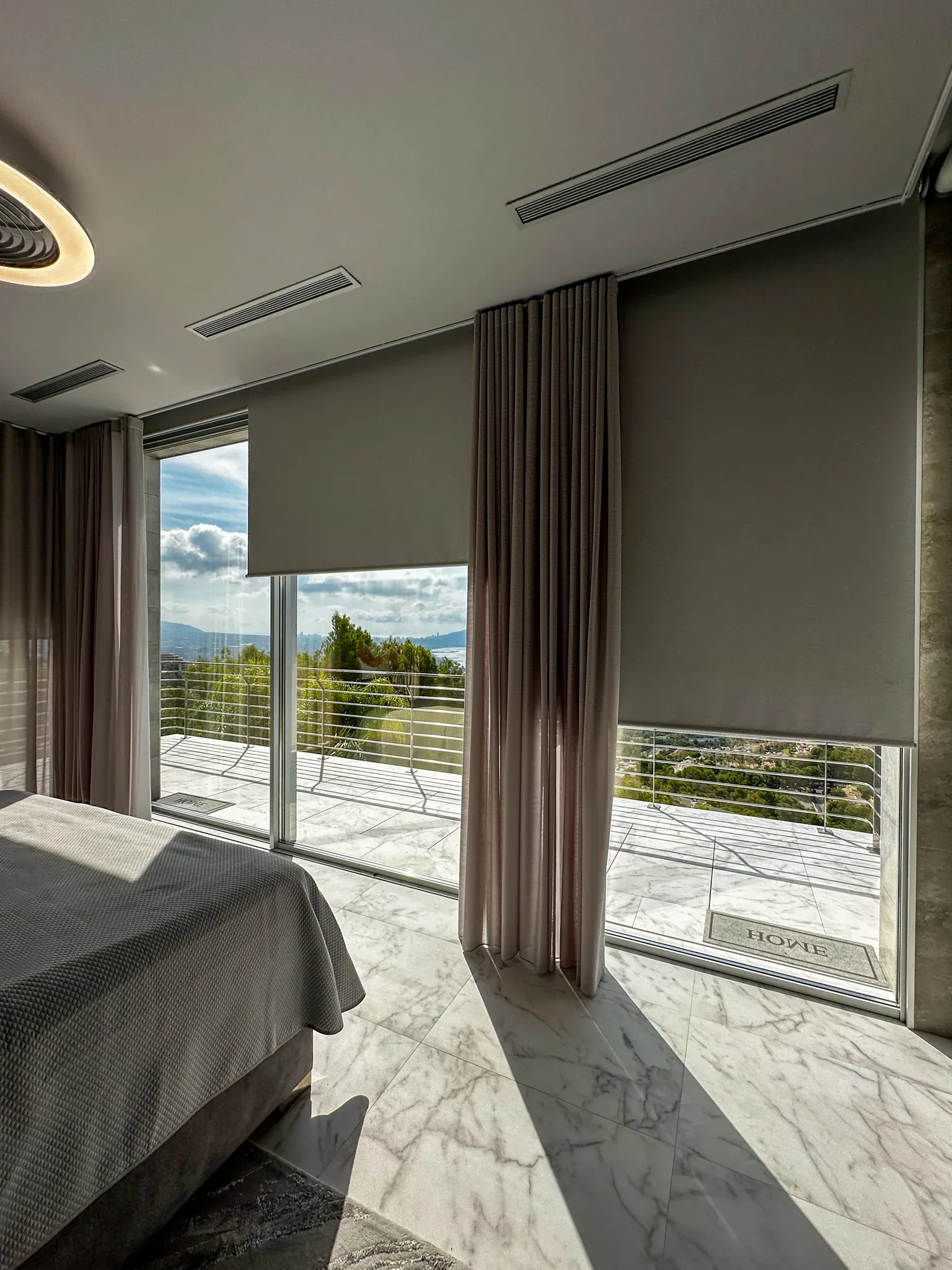 Dormitorio de una villa en la Costa Blanca con estor y cortina a medida frente a un gran ventanal con vistas al mar y las montañas