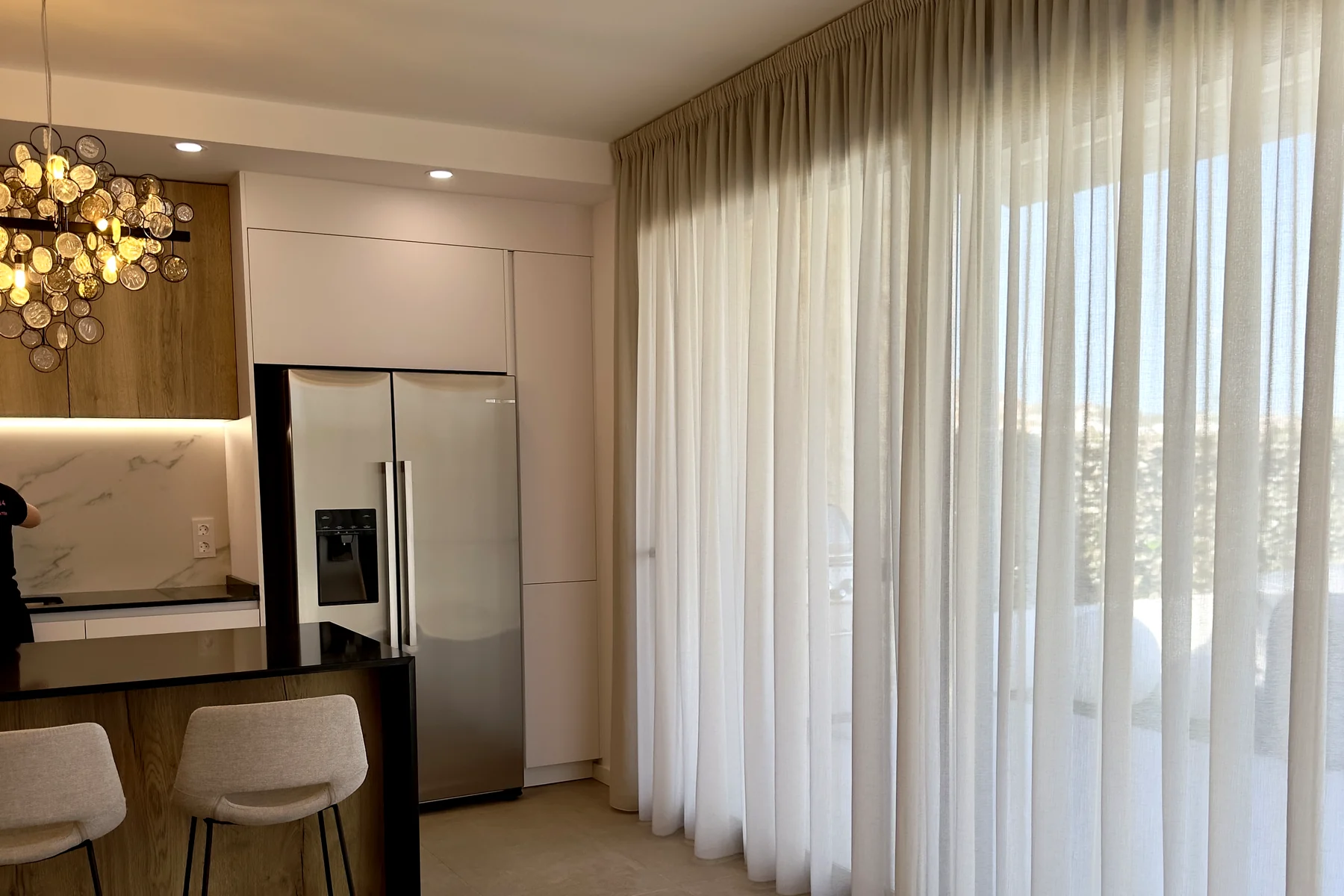 Cocina abierta al comedor con visillo blanco a medida cubriendo el ventanal