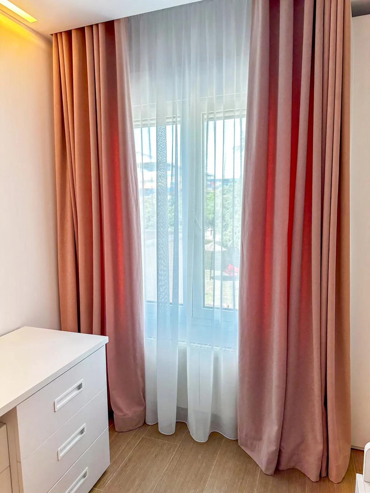Cortinas en tono coral combinadas con visillo en un dormitorio