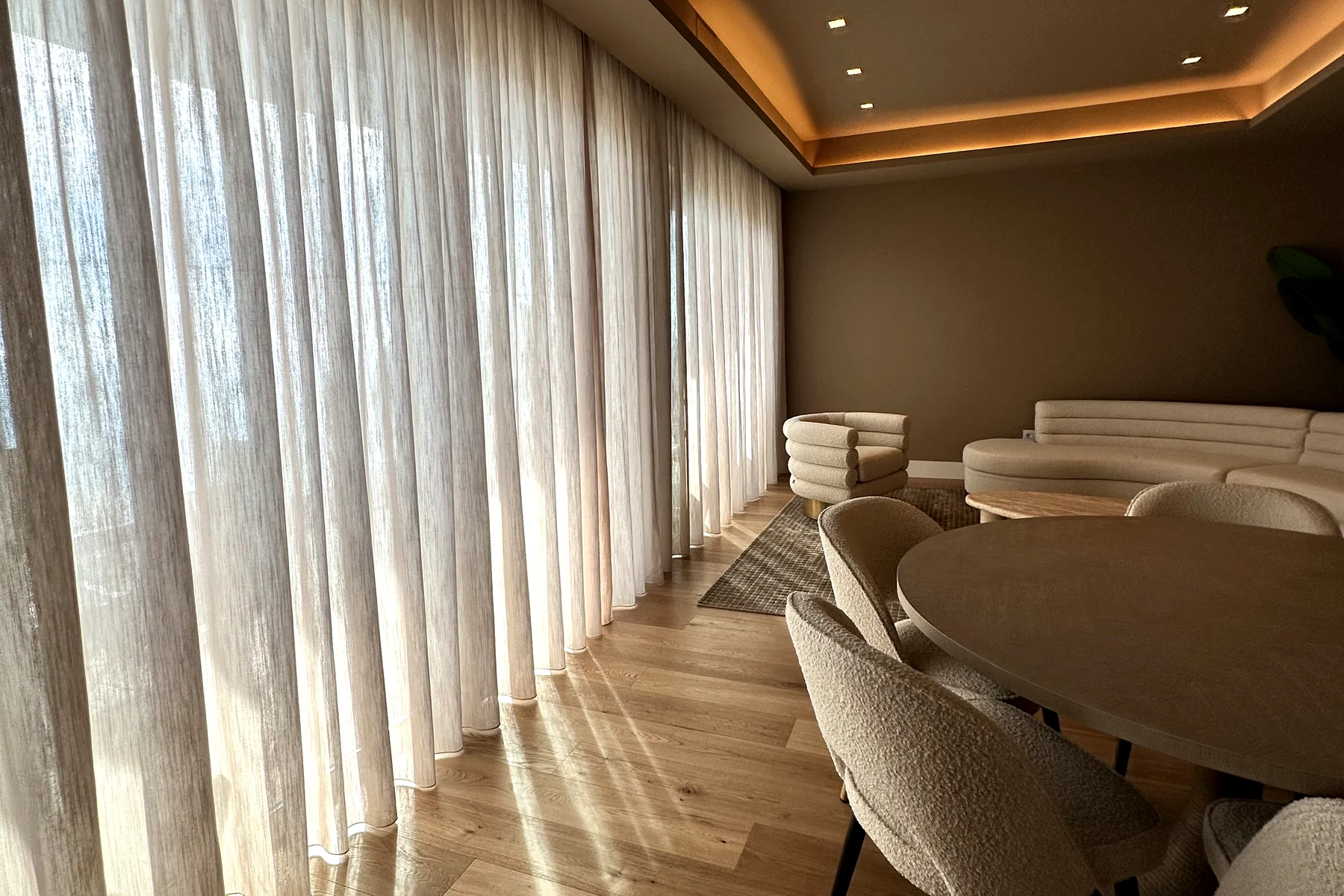 Salón comedor con visillo filtrando la luz en un ventanal de gran altura